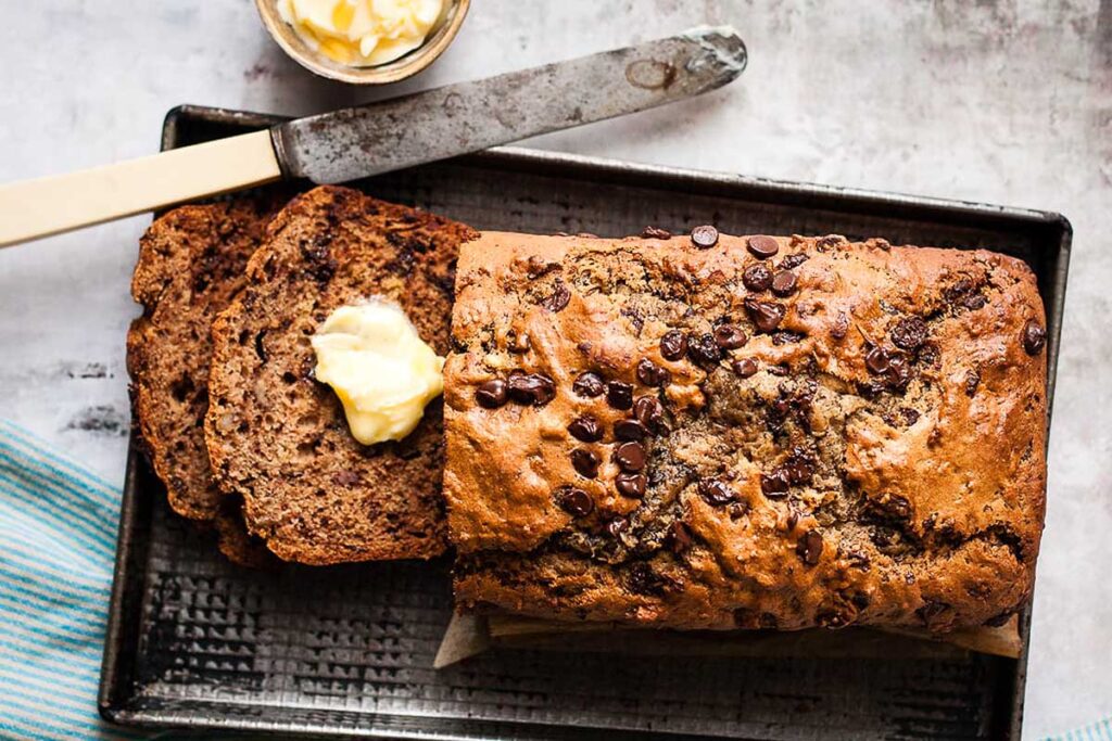 Sour Cream Chocolate Chip Banana Bread on a platter topped wit butter.