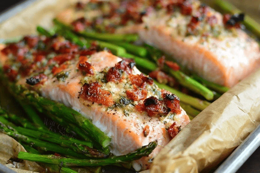 A close up image of a sheet pan with Sun Dried Tomato Lemon Baked Salmon and Asparagus.