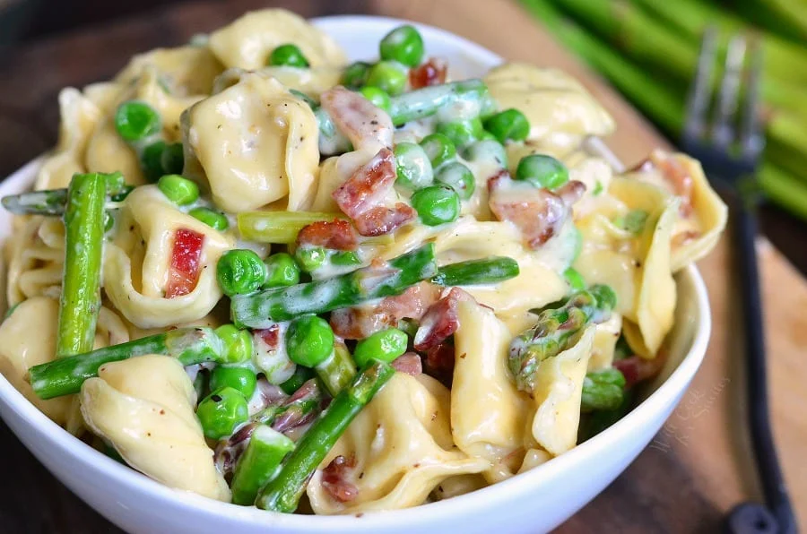 A close up image of a bowl full of Creamy Spring Tortellini with Peas Asparagus and Bacon.