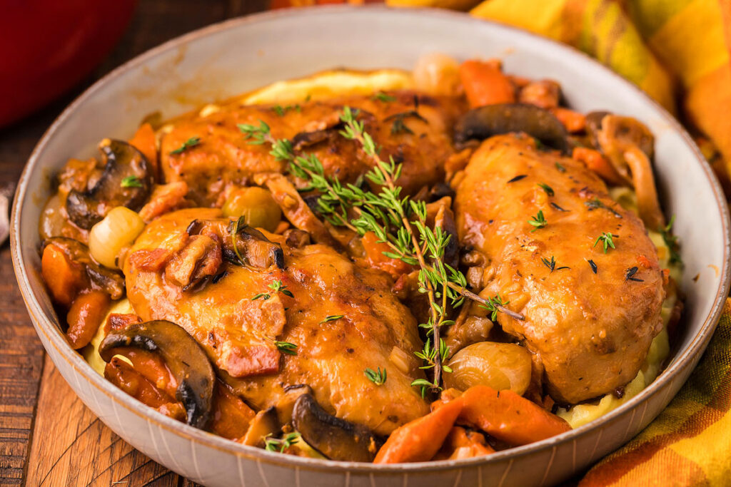 A close up image of chicken and veggies in a red wine sauce in a pot.