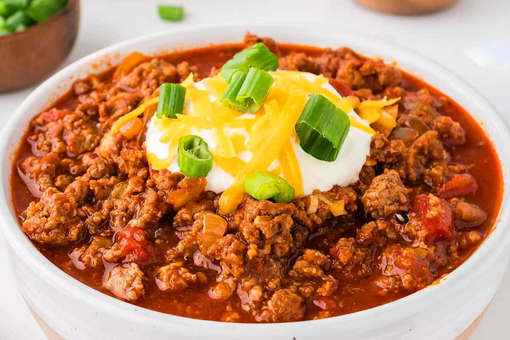 A close up image of a bowl of Crockpot Sausage & Ground Beef Chili topped with sour cream and green onions.