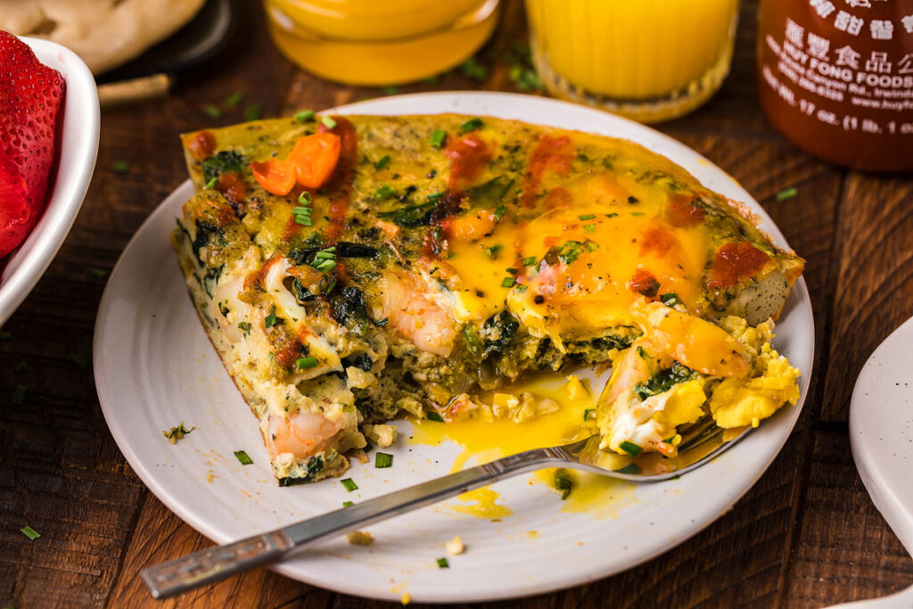 Shrimp Spinach Sunny Side Up Omelette on a white plate with a fork.