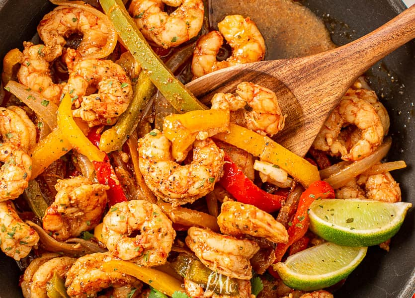 Shrimp and peppers in a skillet with serving spoon.