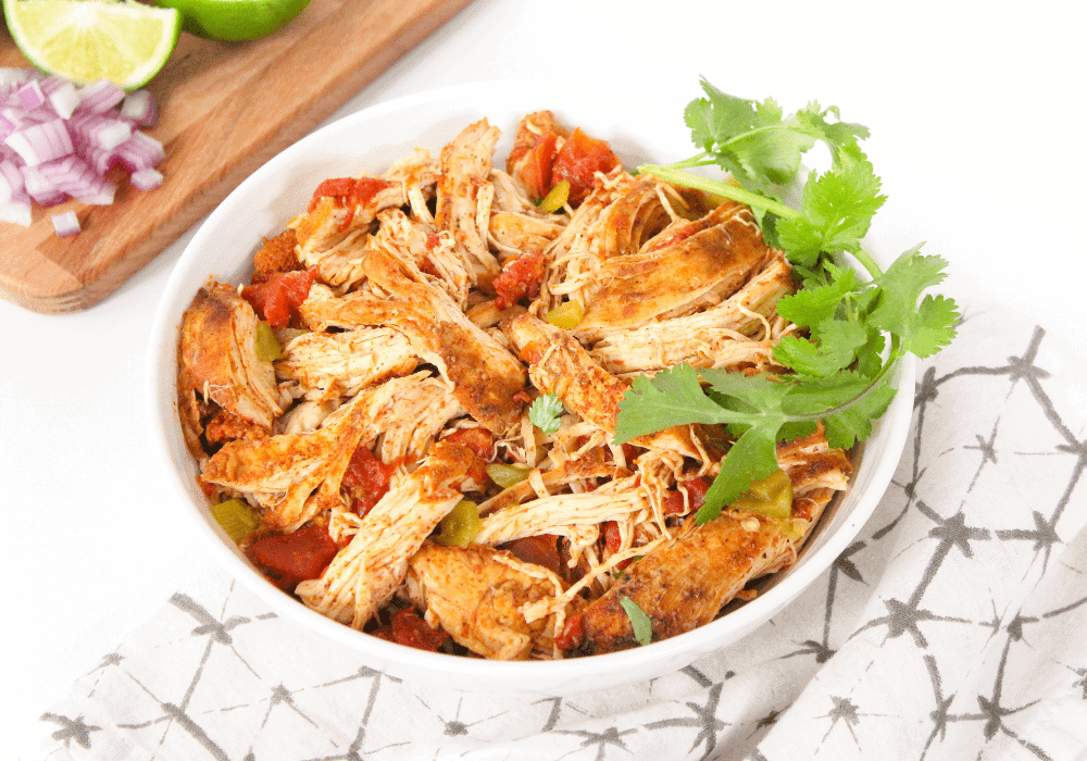 A white bowl with shredded chicken, diced tomatoes, and green chilis.