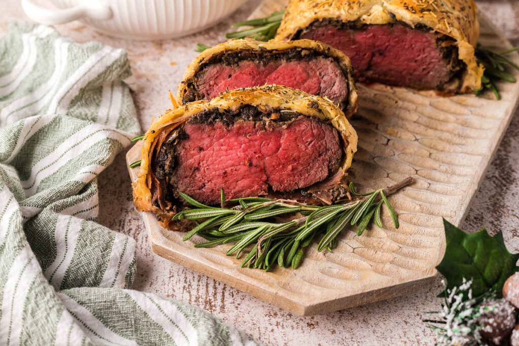 Sliced Beef Wellington on a platter with rosemary.