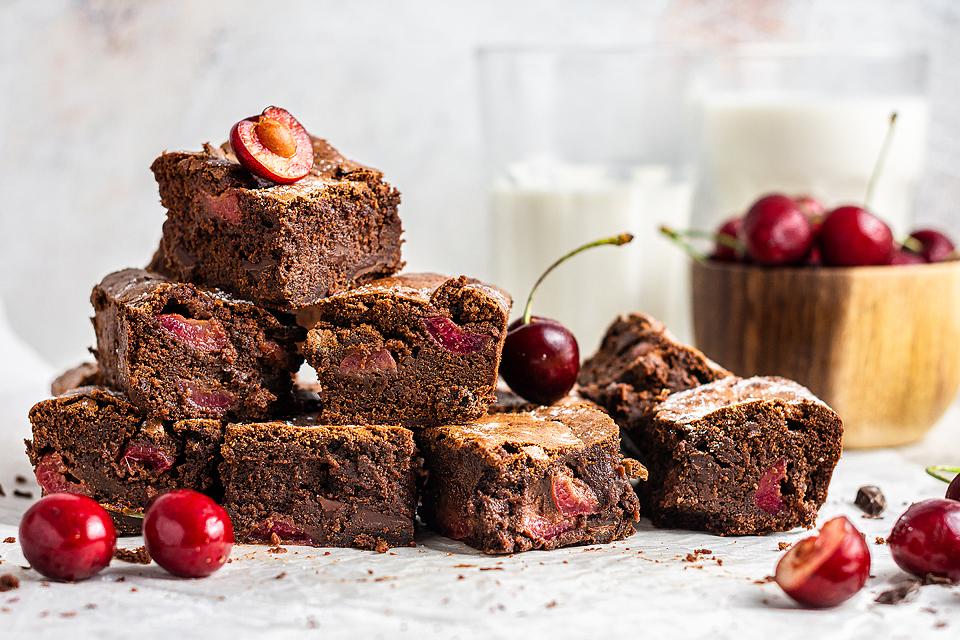 A platter of many Double Chocolate Cherry Brownies with fresh cherries around the stack.