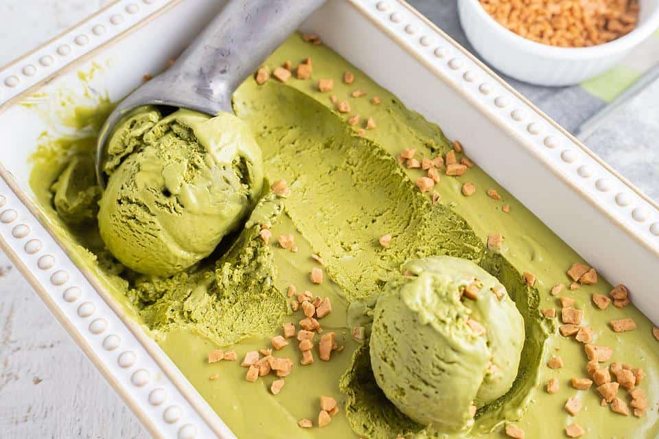 A container of No Churn Matcha Dulce de Leche Ice Cream with an ice cream scoop.