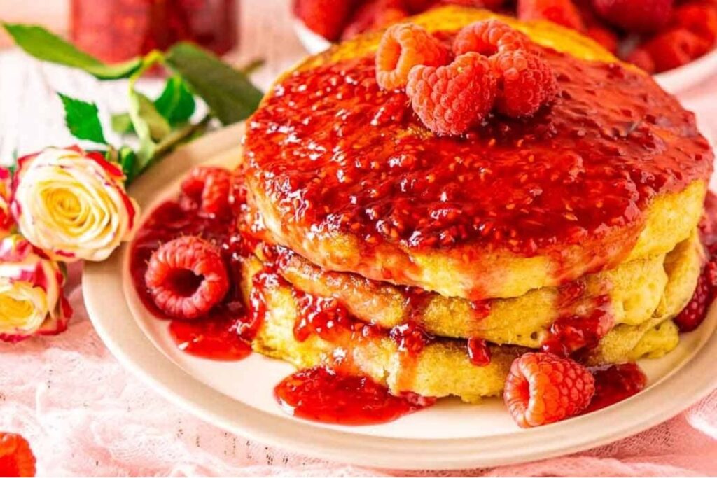 A stack of pancakes topped with raspberry sauce and fresh raspberries.