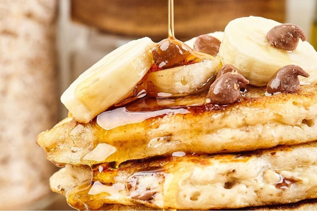 A close up image of a stack of Chocolate Chip Banana Pancakes topped with bananas and chocolate chips.