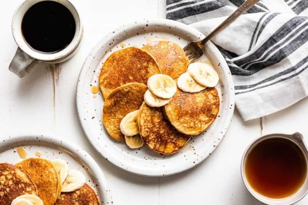 A plate of Healthy Banana Oatmeal Pancakes topped with sliced bananas and syrup.