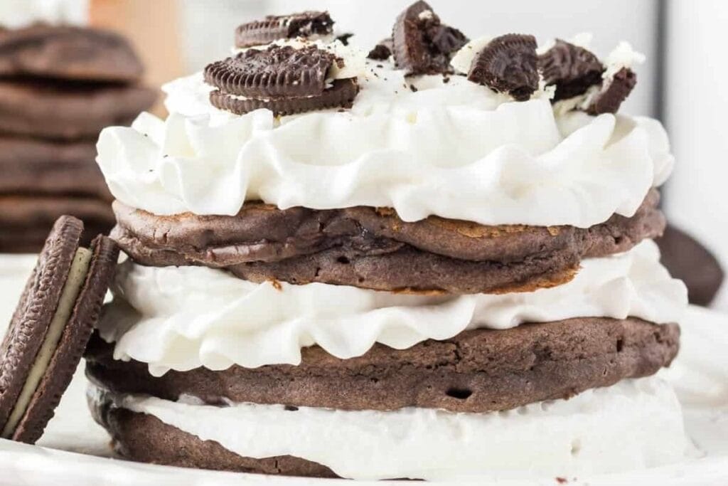 A stack of Oreo Pancakes with whipped cream between each pancake.