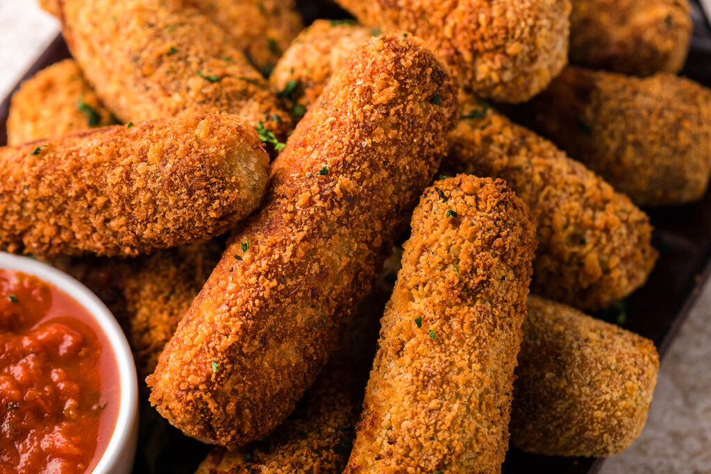 A close up image of Chicken Mozzarella Sticks with a side of tomato sauce.