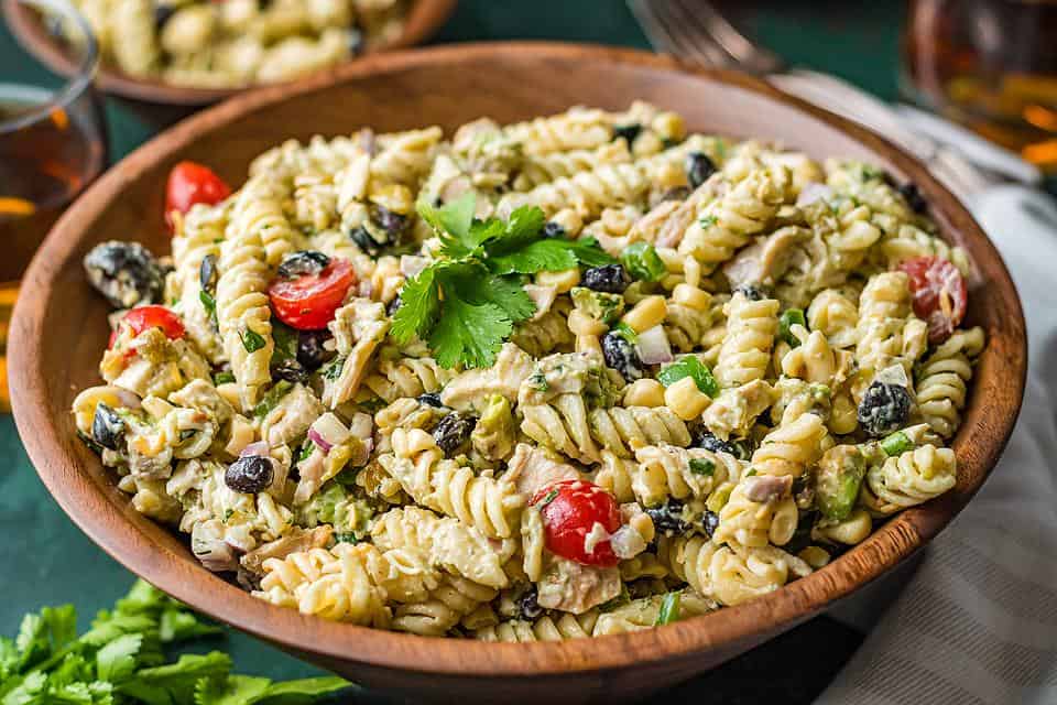 A big bowl of pasta salad with tomatoes and basil as garnish.