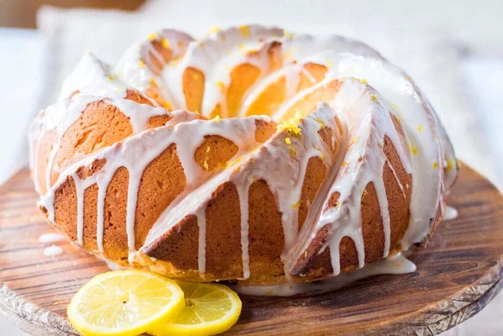 A beautiful Lemon Bundt Cake With Cream Cheese icing and lemon slices on the platter.