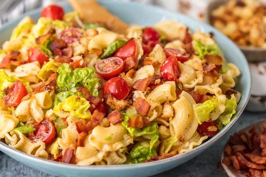 A big bowl of BLT Pasta Salad with extra toppings on the table.