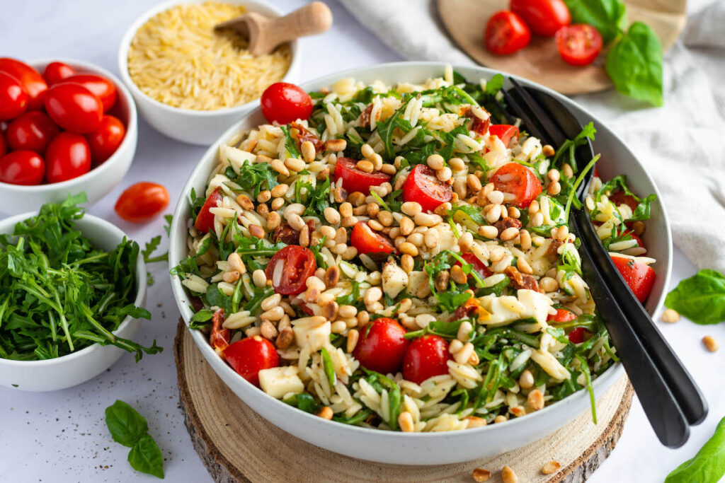 A Mediterranean Orzo Salad in a big white bowl topped with tomatoes.