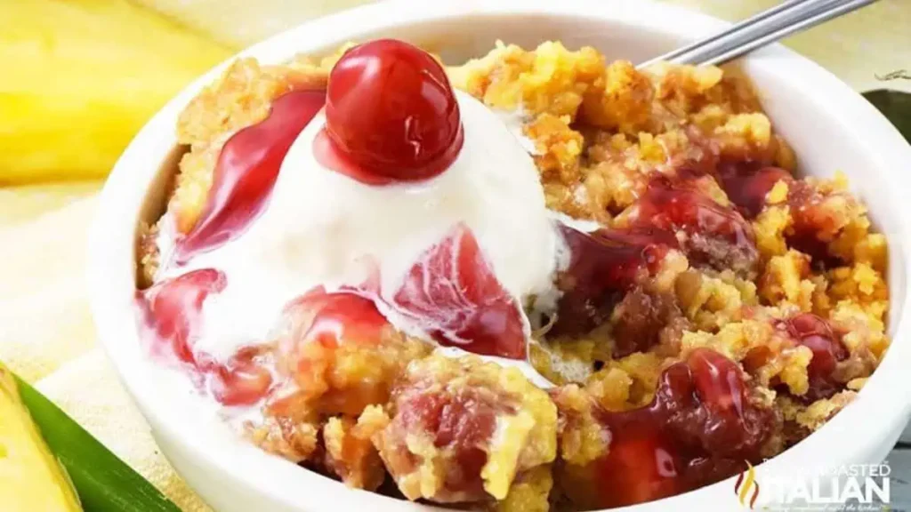 A close up image of a Cherry Pineapple Dump Cake topped with whipped cream and a cherry.