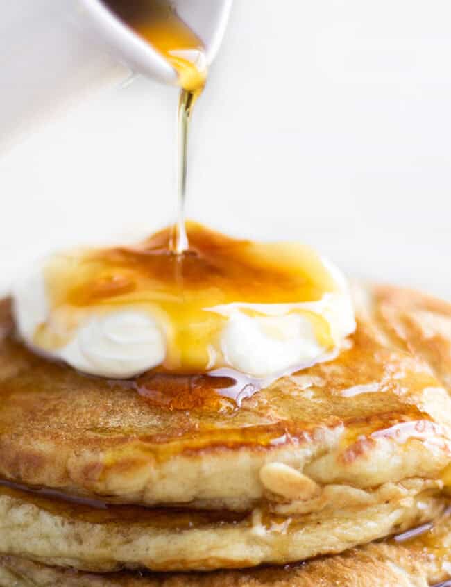 A stack of pancakes on a plate, with Cream and syrup