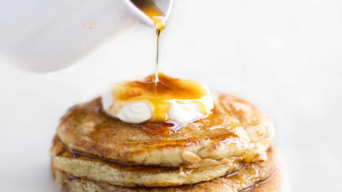 A stack of pancakes on a plate, with Cream and syrup