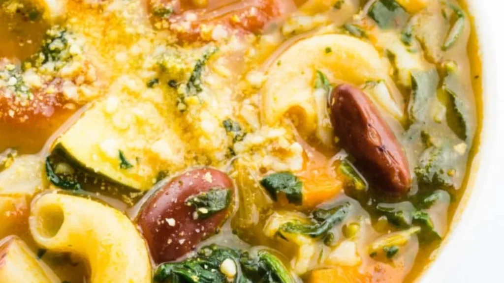  Looking down on a bowl of vegan minestrone, showing spinach, noodles, kidney beans, and veggies. 