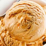 A close-up of a bowl of salted caramel ice cream with a smooth, creamy texture. A metal spoon is partially visible, scooping into the ice cream. The background is minimal, emphasizing the rich details of this delectable salted caramel ice cream recipe.