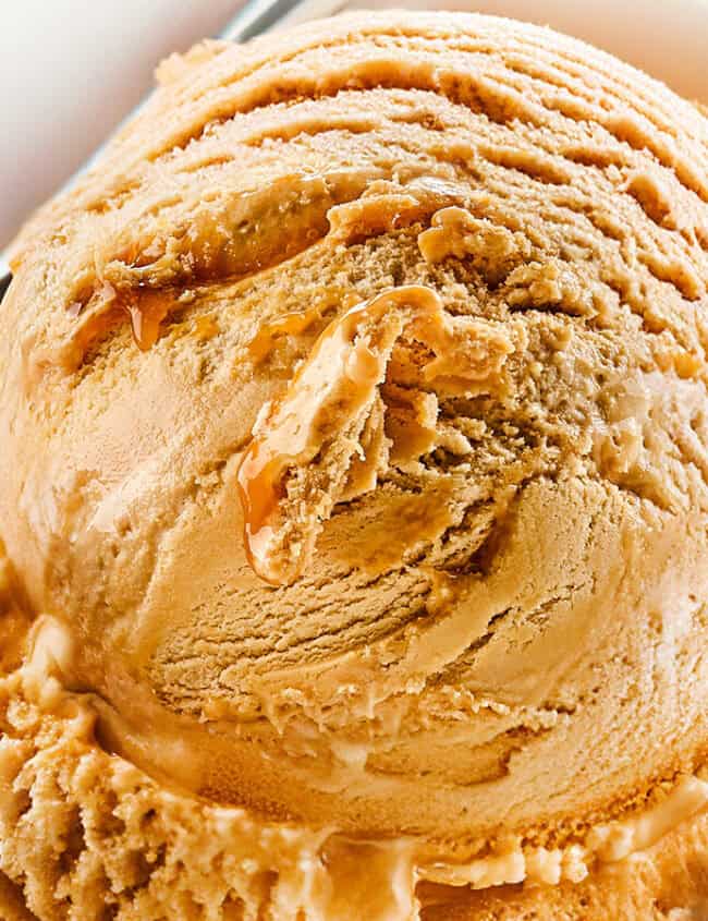 A close-up of a bowl of salted caramel ice cream with a smooth, creamy texture. A metal spoon is partially visible, scooping into the ice cream. The background is minimal, emphasizing the rich details of this delectable salted caramel ice cream recipe.