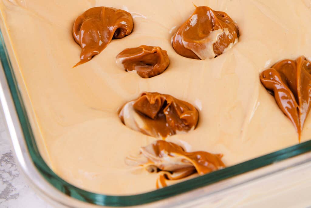 Close-up of caramel being spooned into the ice cream mixture in a glass baking dish. 