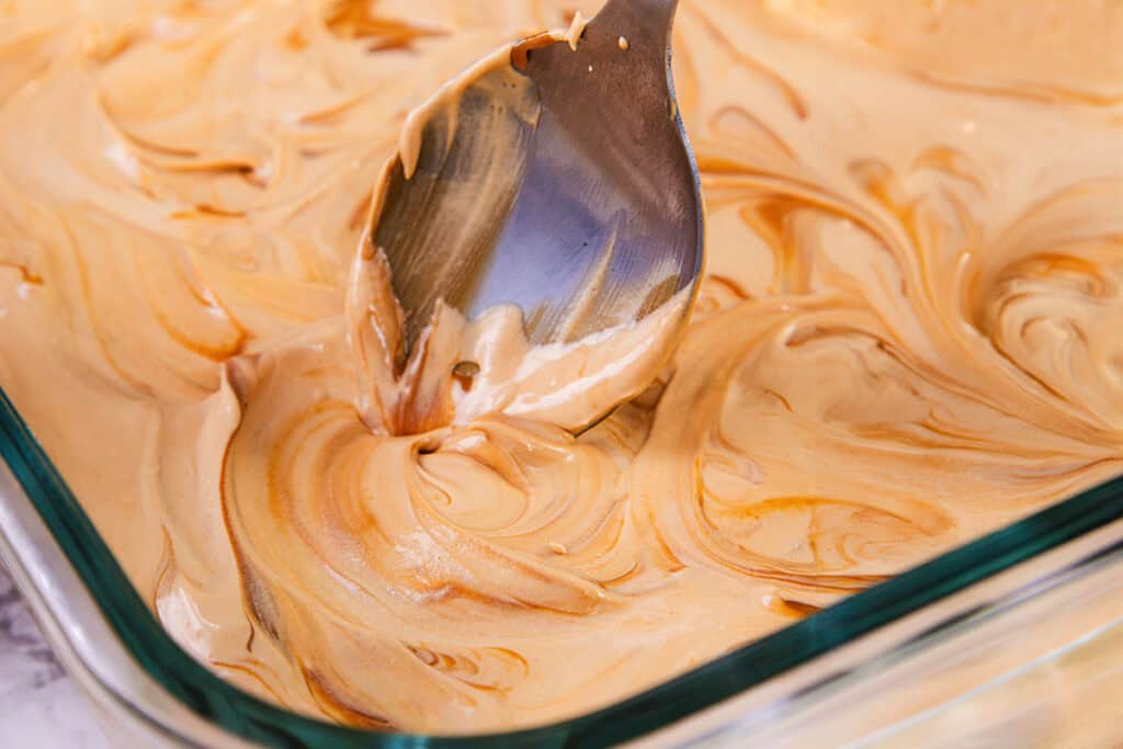 A close-up of a spoon swirling caramel into the ice cream in a glass containe.