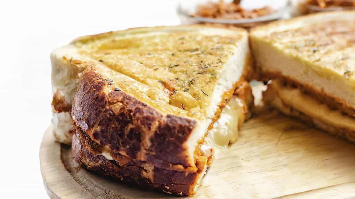 Close-up of a grilled cheese sandwich with melted cheese oozing out from between thick slices of toasted bread. The sandwich is cut in half showing the oozing cheese filling.