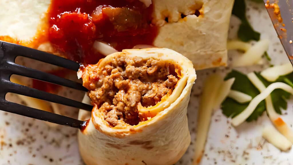 A close-up shot of a Beef Taquito filled with seasoned ground meat. A fork is holding a cut section of the Beef Taquito to show its savory filling. 