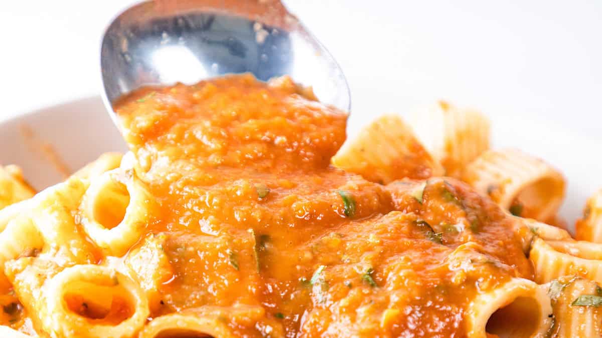 Close-up image of pasta, specifically rigatoni, being topped with a generous amount of tomato sauce from a ladle. The sauce is rich and chunky, with visible bits of herbs, giving the dish a vibrant, appetizing look—an ideal choice for easy dinner recipes.