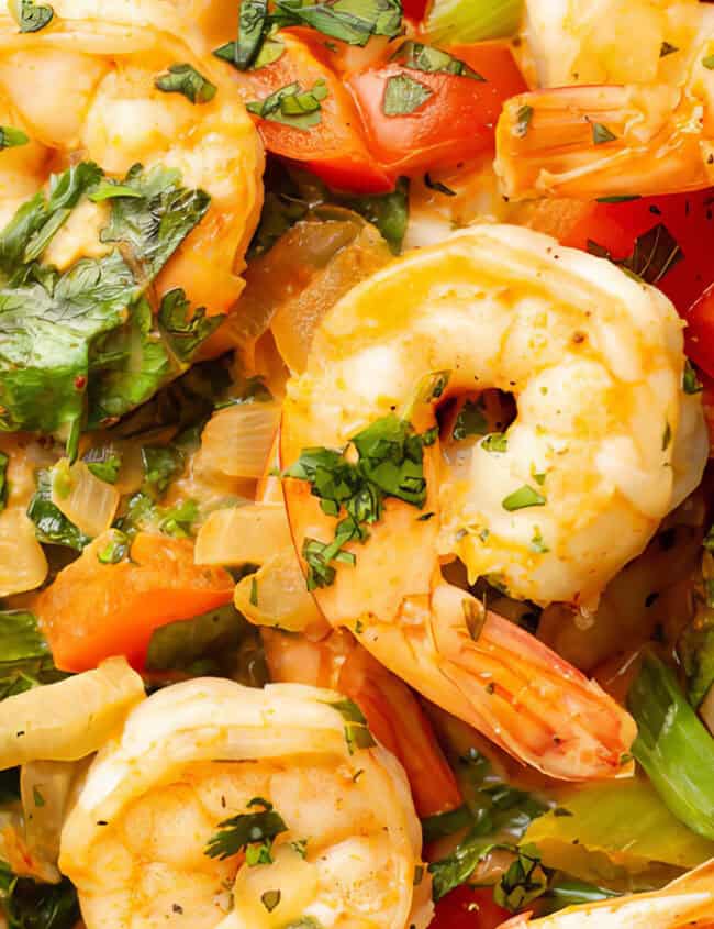 Close-up shot of a colorful shrimp dish featuring large, cooked shrimp, red bell peppers, green snap peas, and chopped fresh herbs. The meal is garnished with a lime wedge and served in a rich, creamy sauce—an enticing addition to your favorite Shrimp Recipes collection.