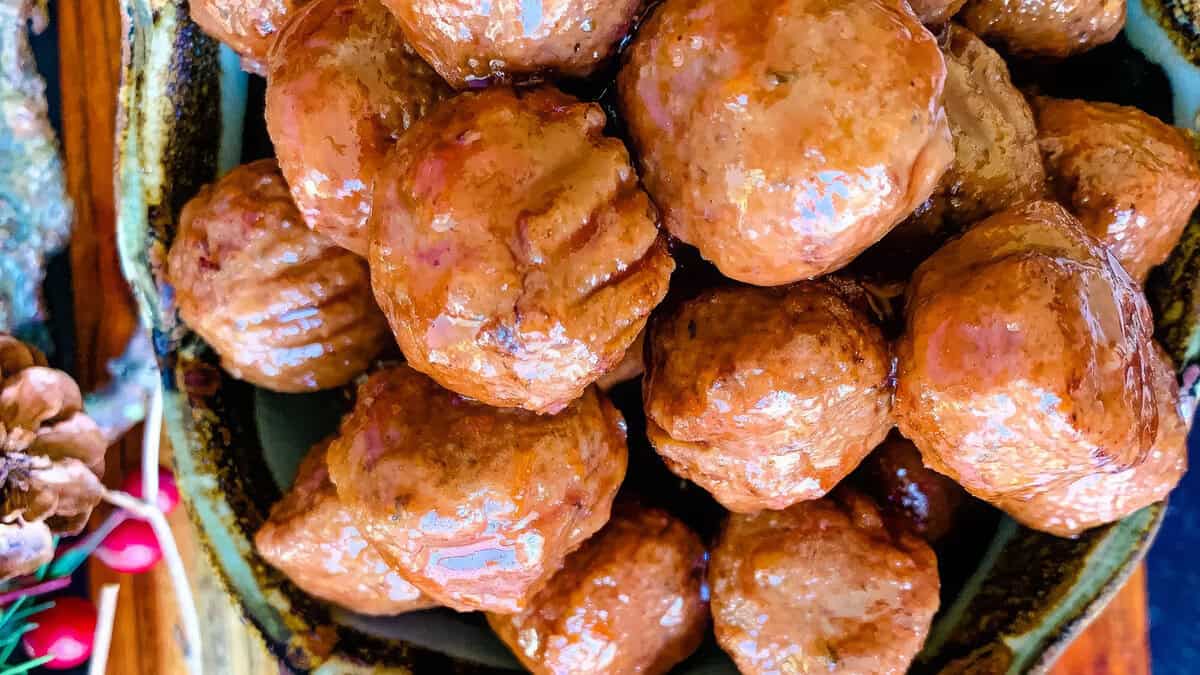 A close-up of a bowl filled with glazed meatballs. The Meatball Magic shines through each one with a glossy, caramelized coating, tightly packed in the bowl. The dish appears to be freshly prepared, with a golden-brown color and a deliciously appetizing look.