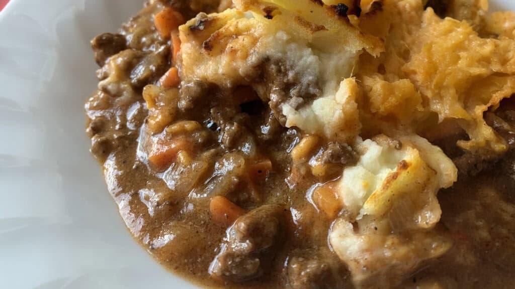 A close-up of shepherd's pie, a star among ground beef recipes, shows a creamy mashed potato topping, slightly browned and crispy in spots, covering a rich and hearty meat filling with bits of vegetables like carrots in a savory brown gravy. The dish appears freshly baked and appetizing.