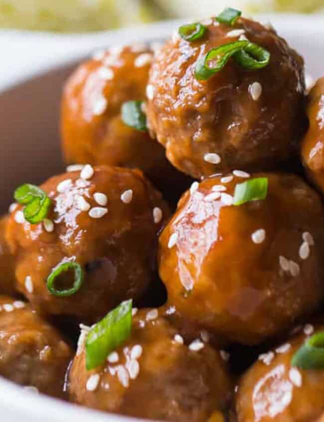 A close-up shot of a bowl filled with glazed meatballs, featuring a delicious ground beef recipe. The meatballs are garnished with sesame seeds and chopped green onions, arranged neatly, with the glaze giving them a shiny appearance.