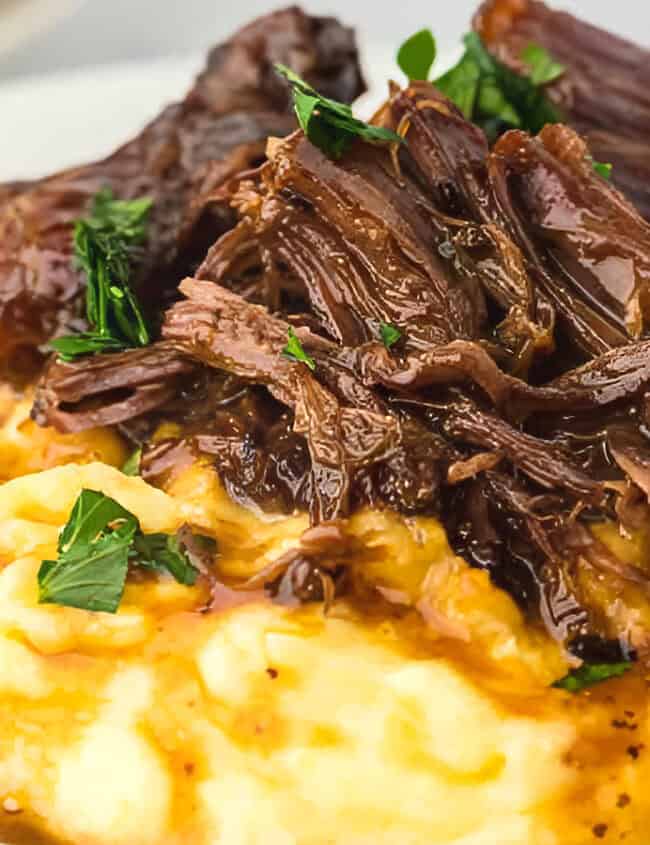 A close-up of a savory dish featuring tender, slow-cooked beef served over creamy mashed potatoes. The beef is garnished with fresh parsley and is accompanied by a rich, flavorful gravy that seeps into the mashed potatoes - perfect for those who love slow cooker recipes.