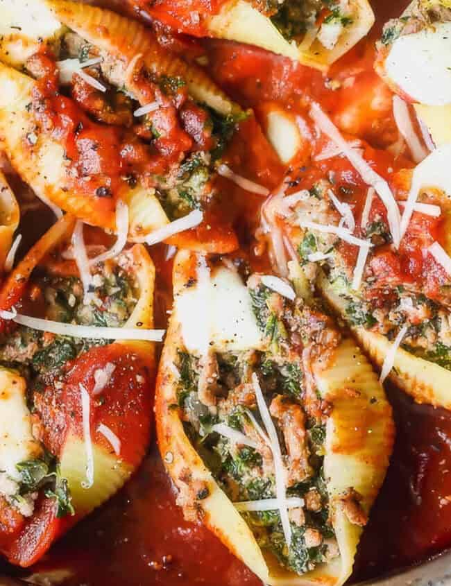 A close-up of a dish featuring large pasta shells stuffed with a mixture of ground beef and spinach, generously covered in tomato sauce and sprinkled with shredded cheese. The dish appears baked and garnished with fresh herbs and grated parmesan, making it a standout among ground beef recipes.