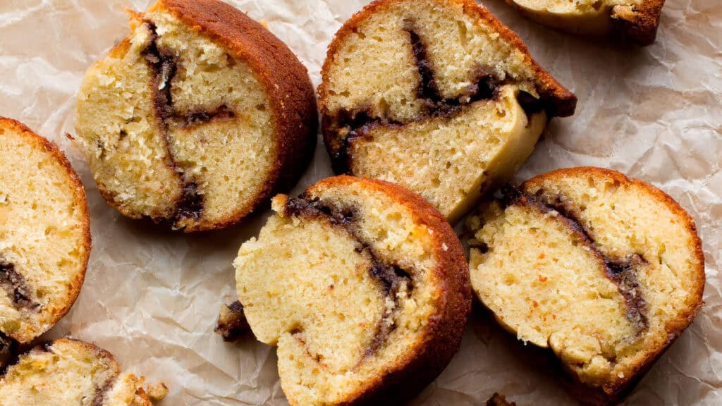 Slices of cinnamon swirl bundt cake are arranged on a piece of crumpled parchment paper. The moist yellow cake has dark cinnamon swirls inside, creating a spiral pattern in each slice. The golden-brown crust contrasts with the light yellow cake interior, a highlight among Bundt Cake Recipes.