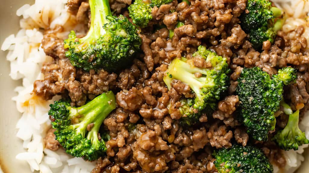 A close-up of a dish featuring steamed white rice topped with cooked ground beef and broccoli, all drizzled in a savory brown sauce. This Ground Beef Recipe looks freshly prepared, with vibrant green broccoli florets contrasted against the rich, seasoned beef.