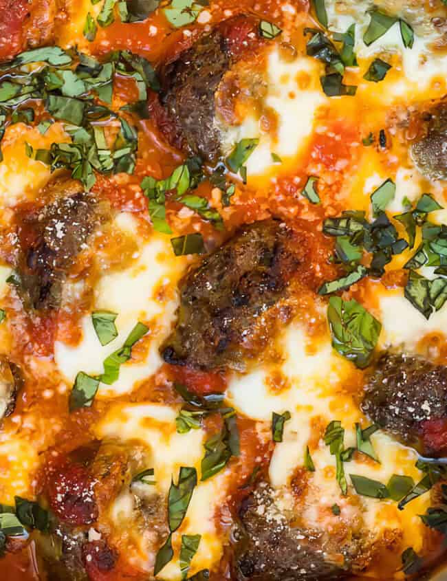 A close-up shot from "Meatball Magic" shows a skillet containing meatballs topped with melted cheese and garnished with chopped fresh basil leaves. The meatballs are covered in rich tomato sauce, and a piece of golden-brown bread can be seen on the side of the plate—perfect for cooking book inspiration.