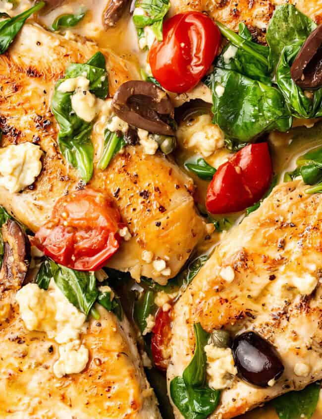 A skillet containing a colorful Mediterranean-inspired dish with juicy chicken breasts, wilted spinach, cherry tomatoes, black olives, and crumbles of feta cheese, all cooked in a rich, flavorful sauce is a perfect example of Mediterranean recipes at their finest.