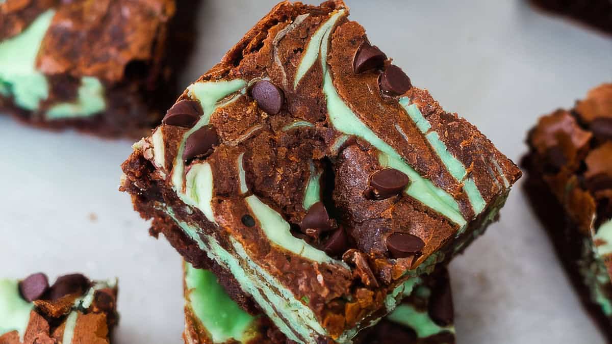 Close-up of a chocolate mint brownie featuring swirls of green mint-flavored batter throughout the chocolate base. The surface is topped with chocolate chips for added texture and richness, perfect for chocoholics. The brownie appears dense and moist with a rich, layered appearance that's beyond basic.