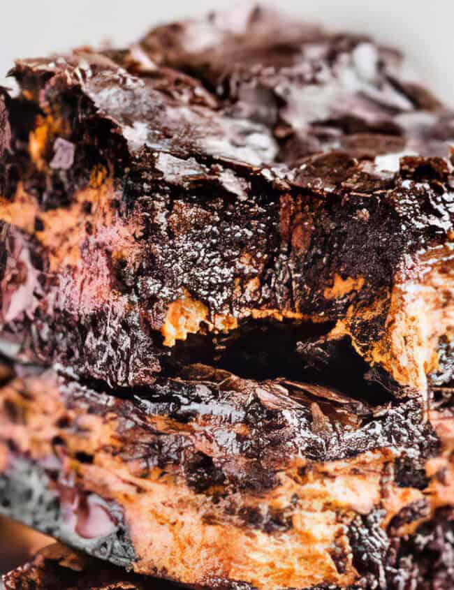 Close-up of a stack of two decadent brownies with a rich, gooey chocolate texture. Perfect for chocoholics, these brownies are layered with a ribbon of additional chocolate or fudge, highlighting their moist and indulgent interior. The background is blurred, emphasizing the beyond basic dessert.