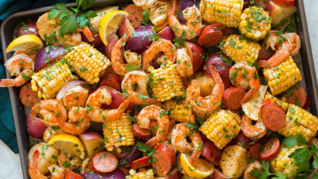 A colorful spread of a seafood boil on a tray, featuring shrimp, sausage slices, corn on the cob pieces, and red potatoes. Garnished with fresh parsley, lemon wedges, and a sprinkling of seasoning—truly one of the finest Southern recipes.