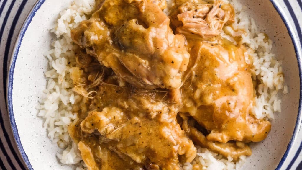 A bowl filled with white rice topped with pieces of chicken covered in creamy brown gravy. The dish appears to be a hearty, homestyle Southern recipe with tender, shredded chicken immersed in the rich, thick sauce, creating a savory and comforting presentation.