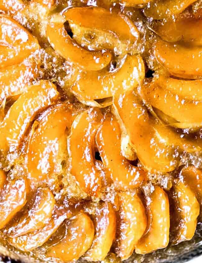 A golden brown upside-down cake with neatly arranged slices of caramelized apples on top. The glossy finish indicates a sugary glaze, making it an appealing and tempting dessert. Ideal for those exploring new dessert recipes, the cake appears moist and is likely freshly baked.