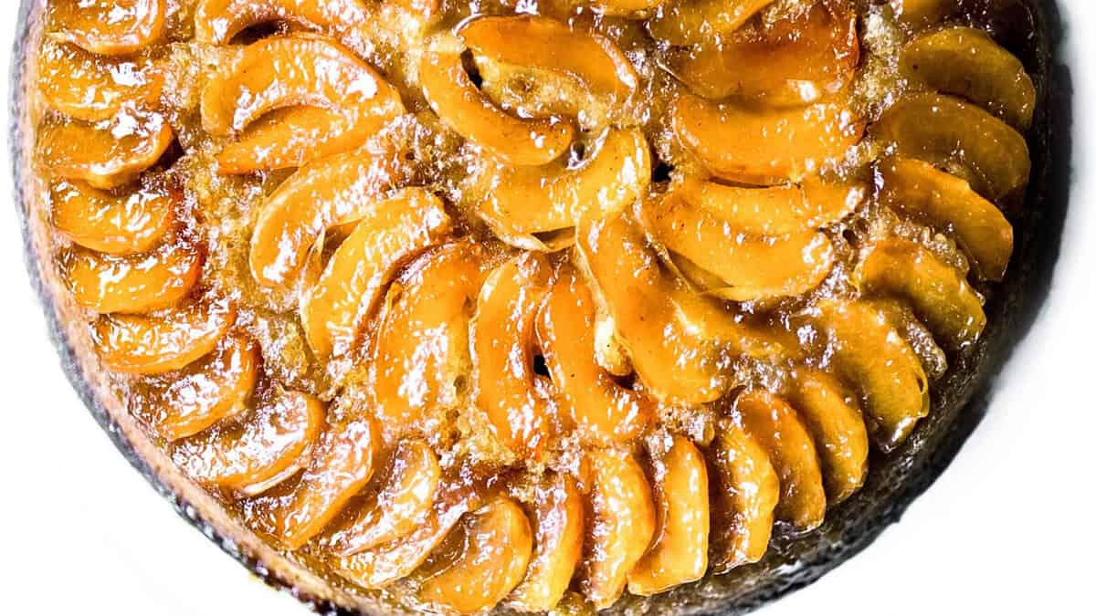 A golden brown upside-down cake with neatly arranged slices of caramelized apples on top. The glossy finish indicates a sugary glaze, making it an appealing and tempting dessert. Ideal for those exploring new dessert recipes, the cake appears moist and is likely freshly baked.