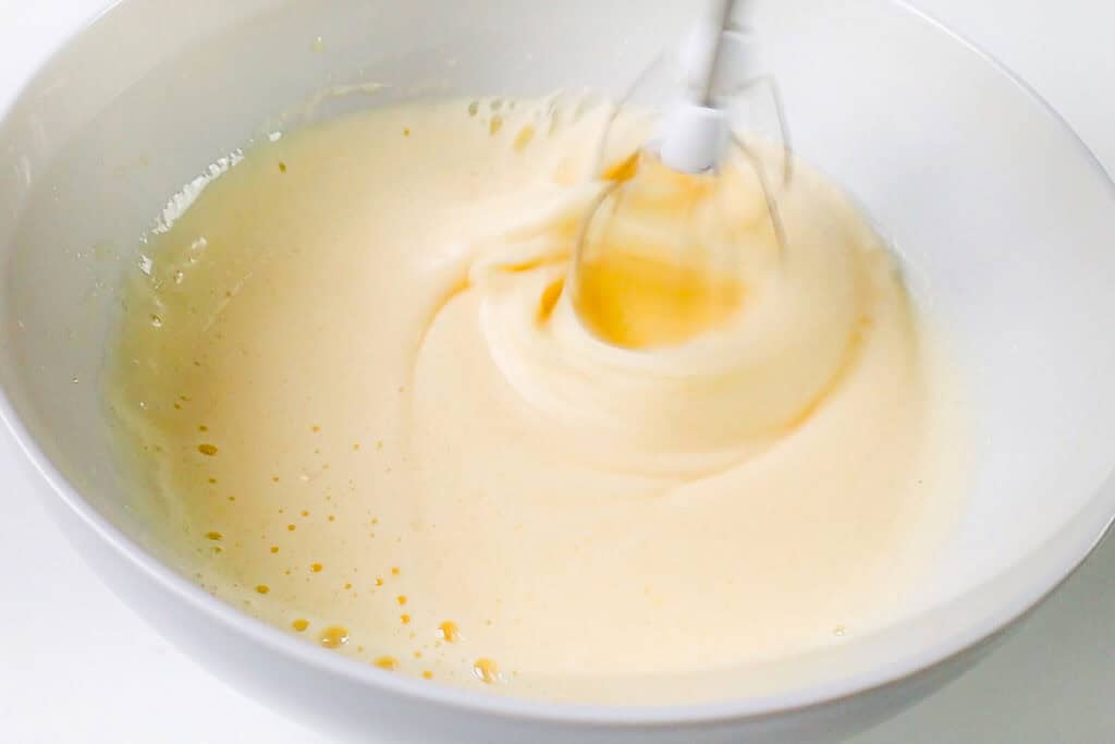 A close-up image of a white bowl with the fluffy mixture of eggs and sugar.