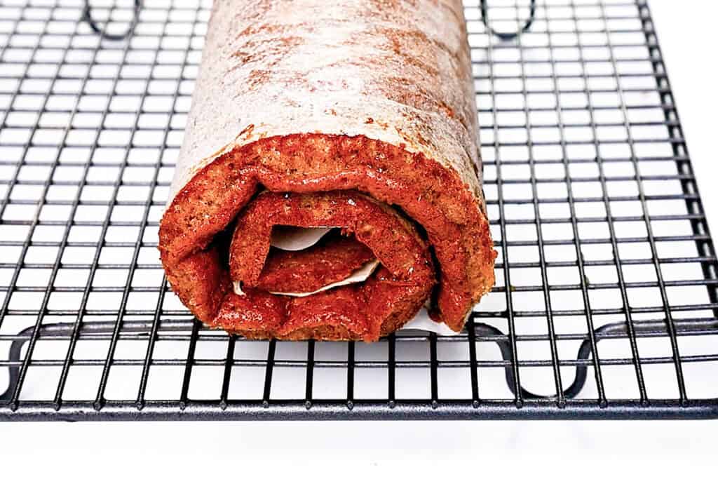 A close-up of a rolled cake positioned on a black cooling rack. 