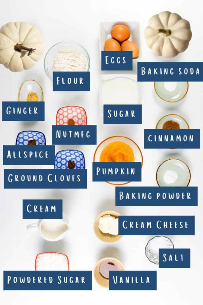 A top-down view of baking ingredients laid out on a white background, perfect for making a Pumpkin Swiss Roll. Items include flour, sugar, eggs, baking soda, baking powder, salt, cream cheese, cream, vanilla, powdered sugar, nutmeg, ginger, allspice, ground cloves, cinnamon, and pumpkin. Each item is labeled.